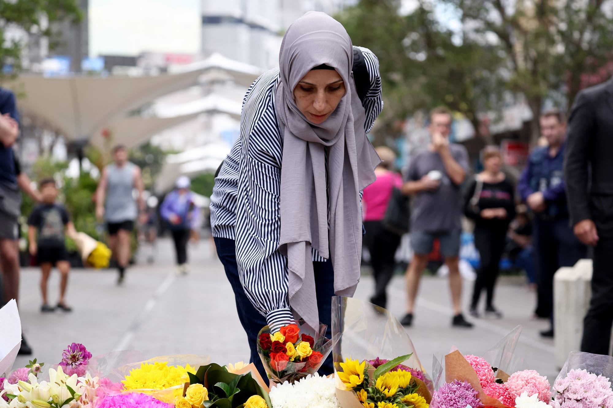 woman lays flowers to pay tribute to the victims of Sydney mall attack