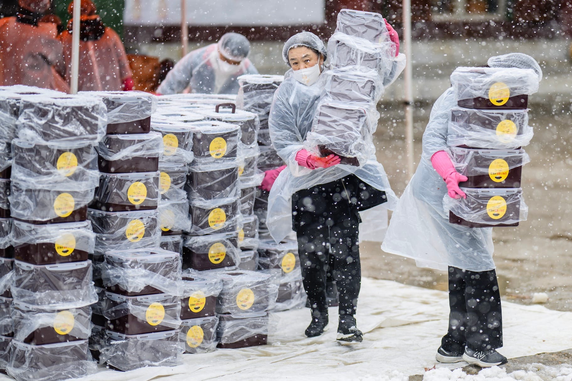 Participants carry boxes of freshly made kimchi, a traditional Korean dish of spicy fermented cabbage and radish, during a kimchi making festival held amid snowfall at the Jogyesa Temple in Seoul on November 27, 2024