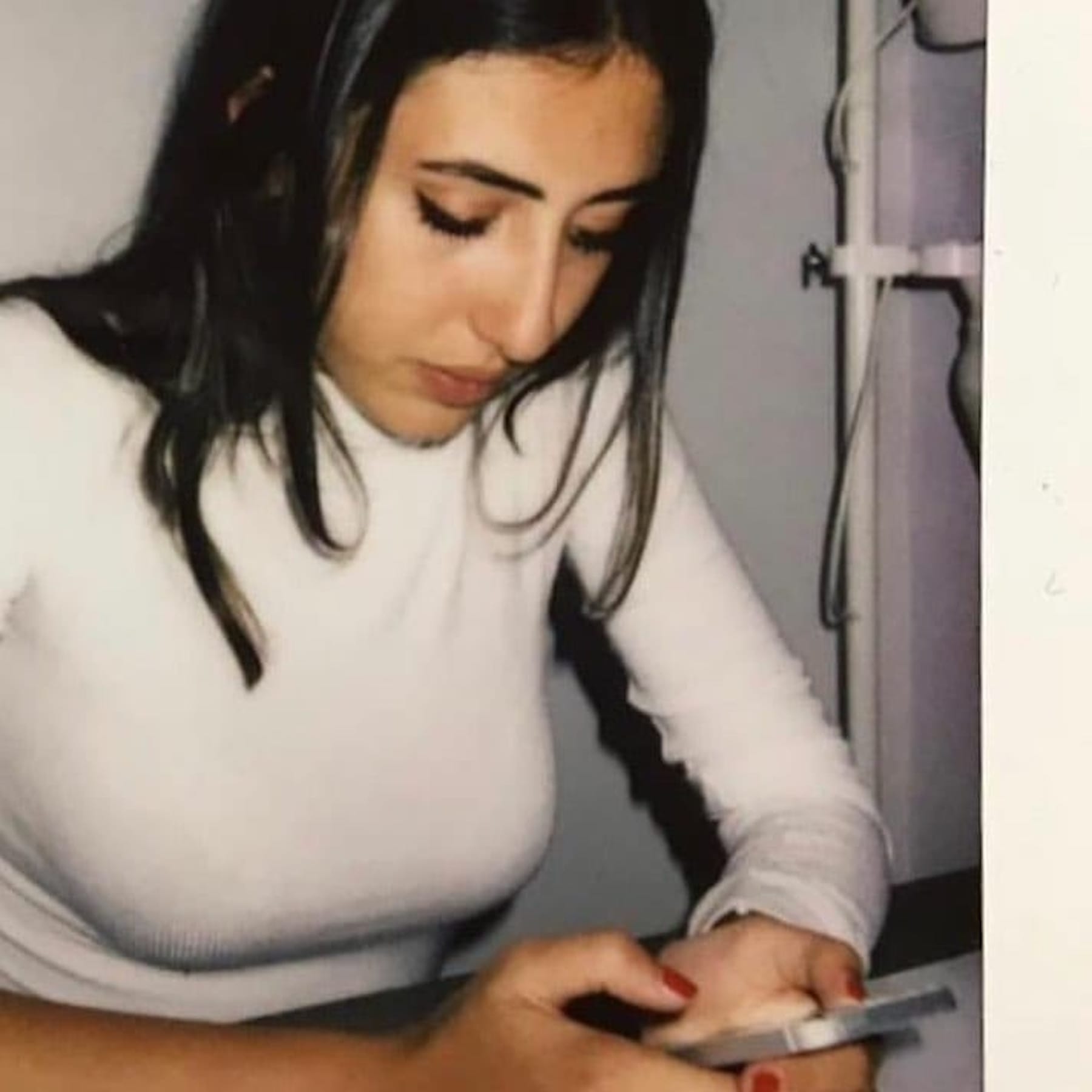 A half side portrait of Cecilia Sala in a white top and looking at her phone.