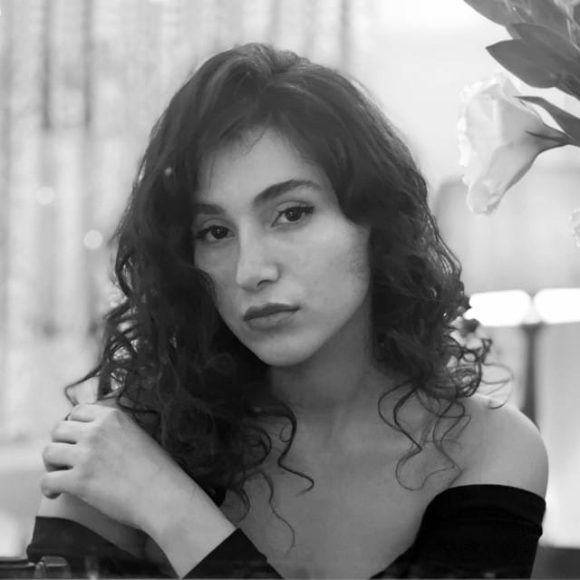 Black-and-white portrait of Iranian woman singer Parastoo Ahmadi, wearing an off-shoulder top and uncovering her hair to defy against dress codes in Iran.