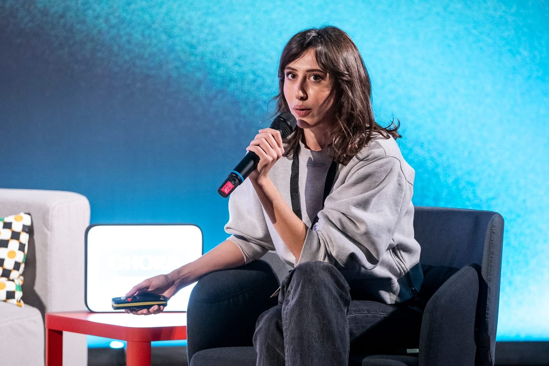 The journalist and writer Mario Calabresi's interview with Cecilia Sala in the presentation of her podcast In Viaggio con Stories at the Milan Conservatory during the Chora Festival. Sala is holding a microphone as she speaks for presentation in a sofa before blue display background..