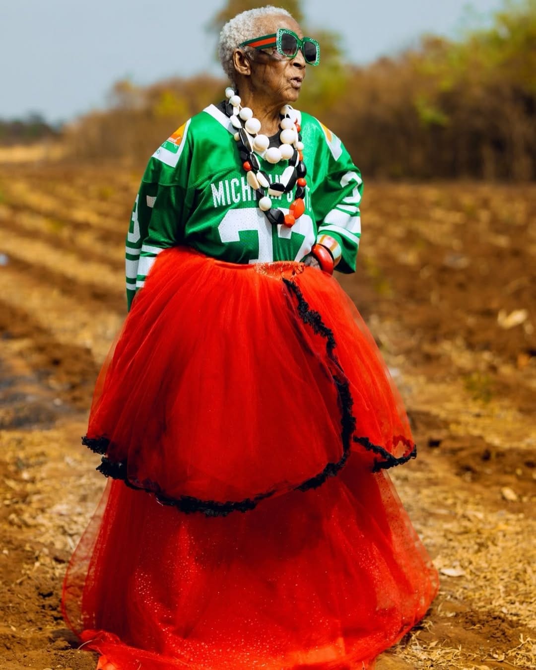 Chola is dressed in a pair of green sunglasses, a green sports top, big marble accessories and a red puffy dress that all together make up the Zambian country flag.