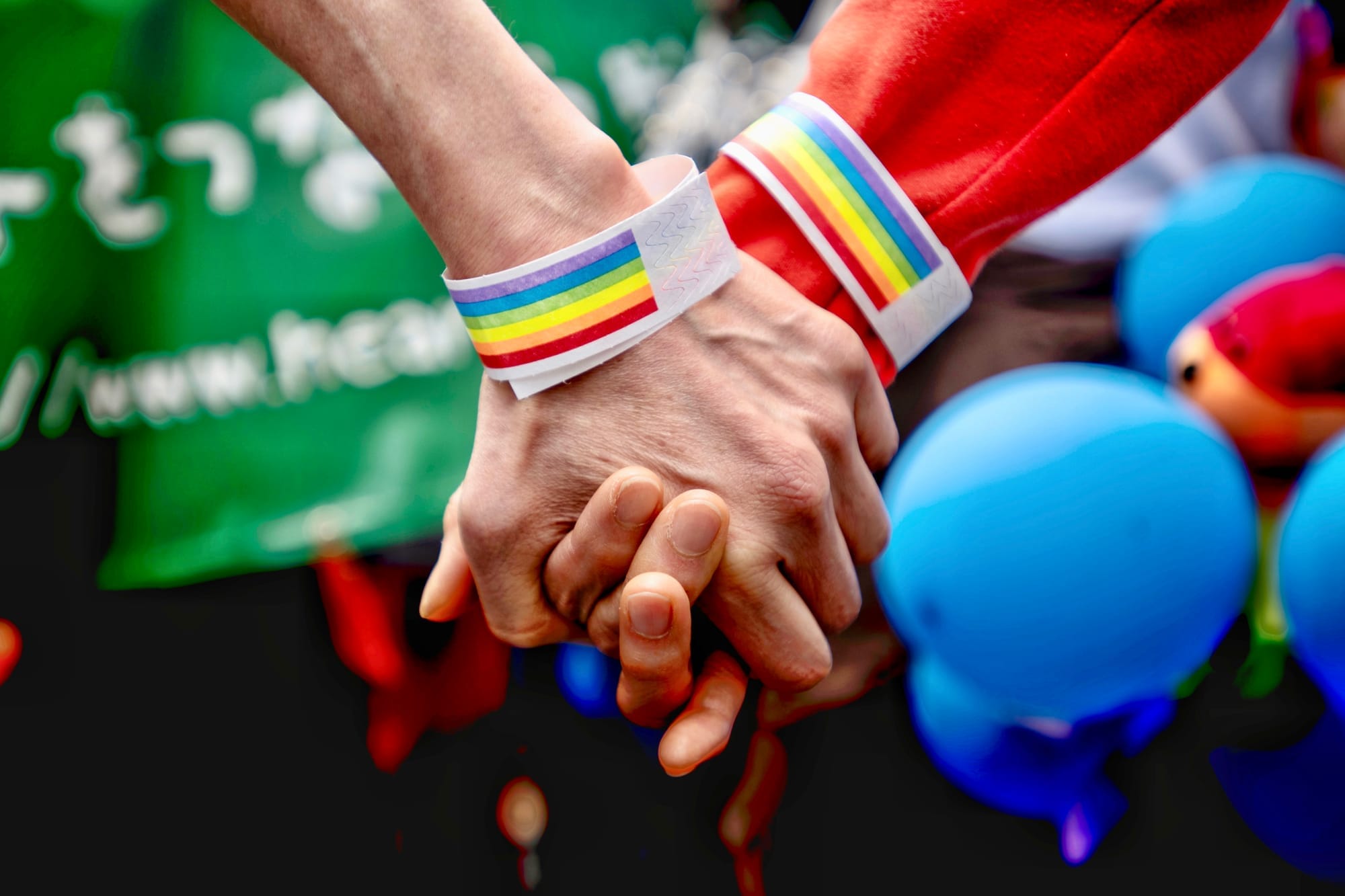 A close shot of two women's wearing rainbow wristbands and holding their hands at the 2019 Tokyo Rainbow Pride parade.