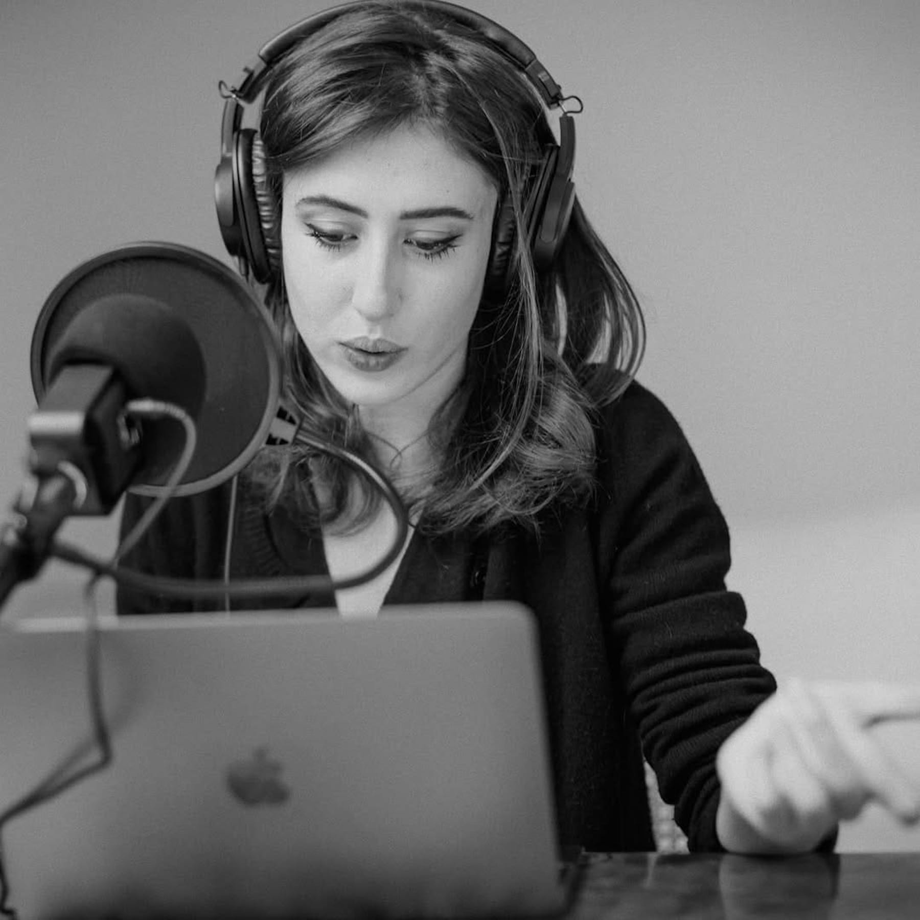 A black and white portrait of Sala recording with a microphone and earphones before her laptop.