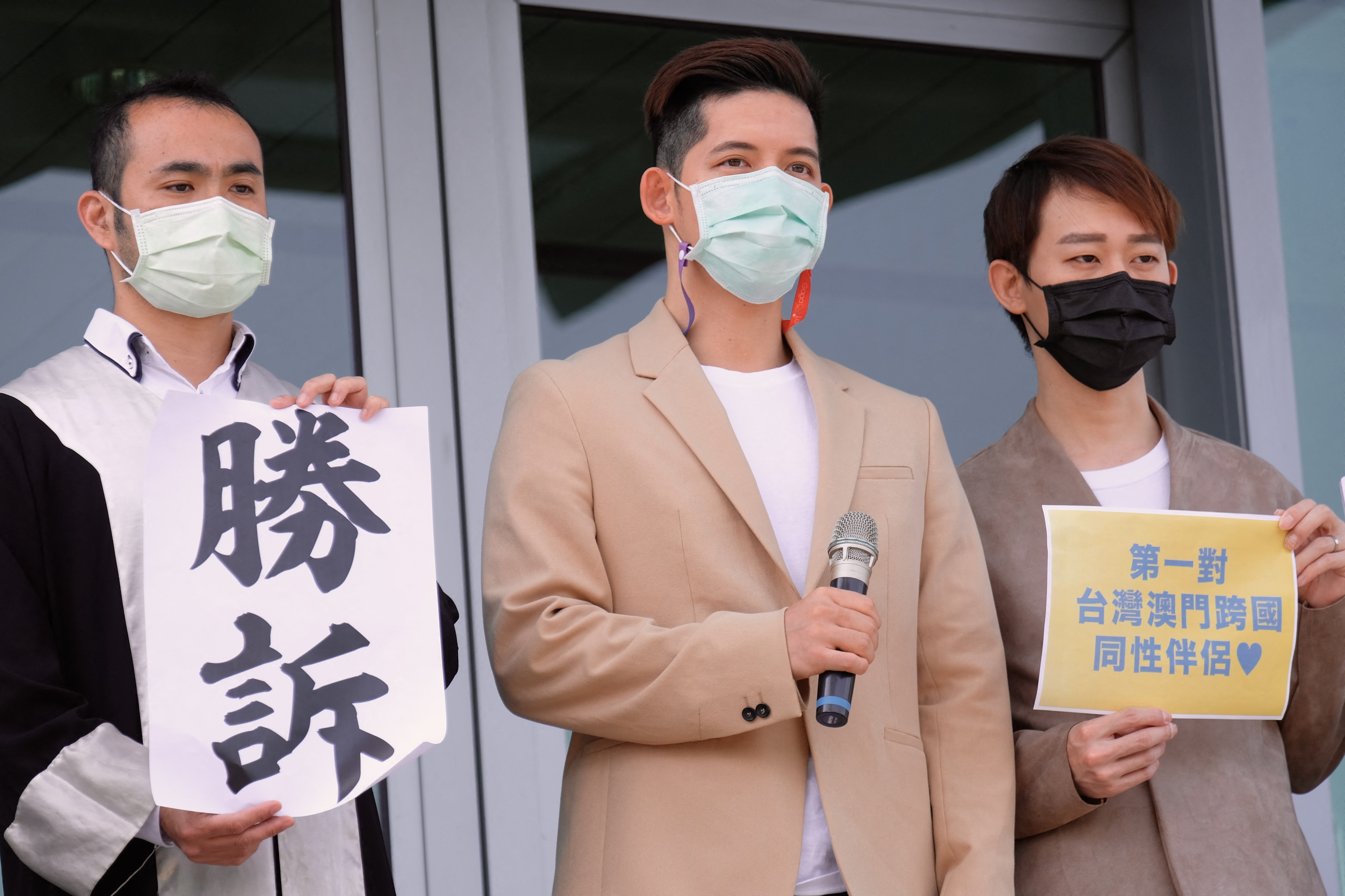 Taiwanese Ting Tse-yen (R) and his Macau same sex partner Leong Chin-fai (C) take part in a press conference in front of Taipei High Administrative Court after winning the lawsuit. The man with lawyers suit holds a sign reading  wins the lawsuit case.