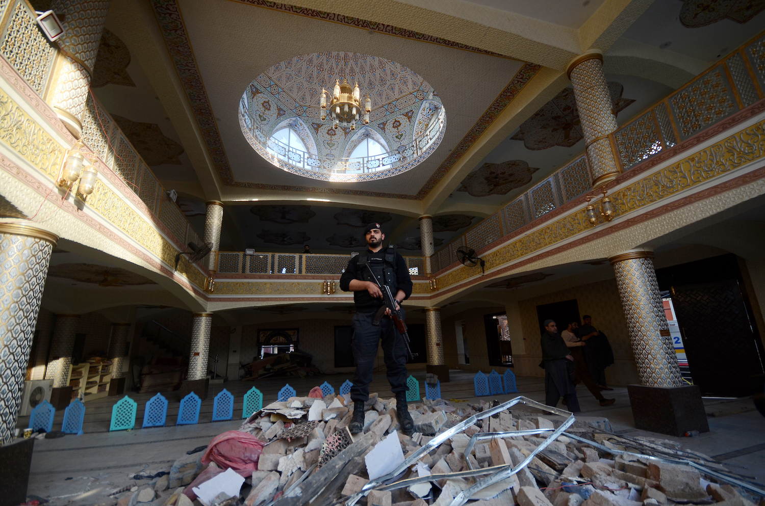 pakistan police standing on the debris in the mosque holding a gun