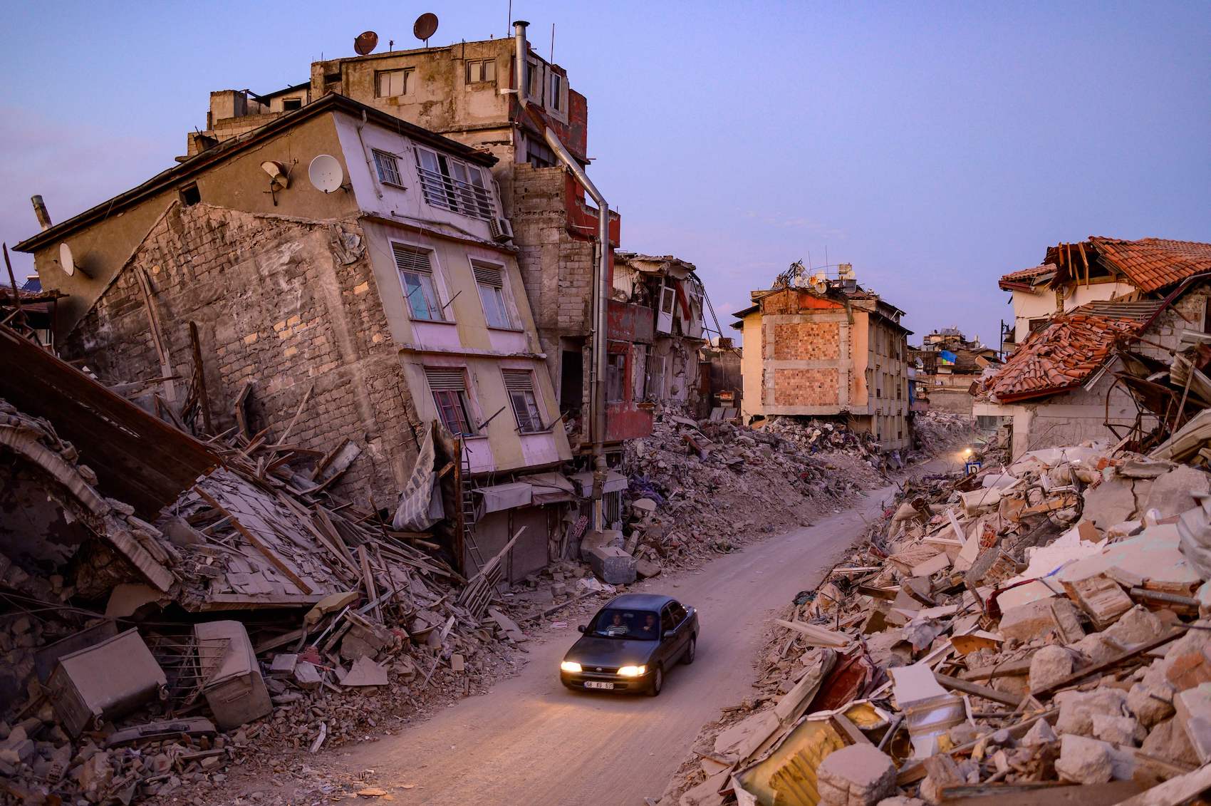 A car drives past collapsed buildings in Antakya