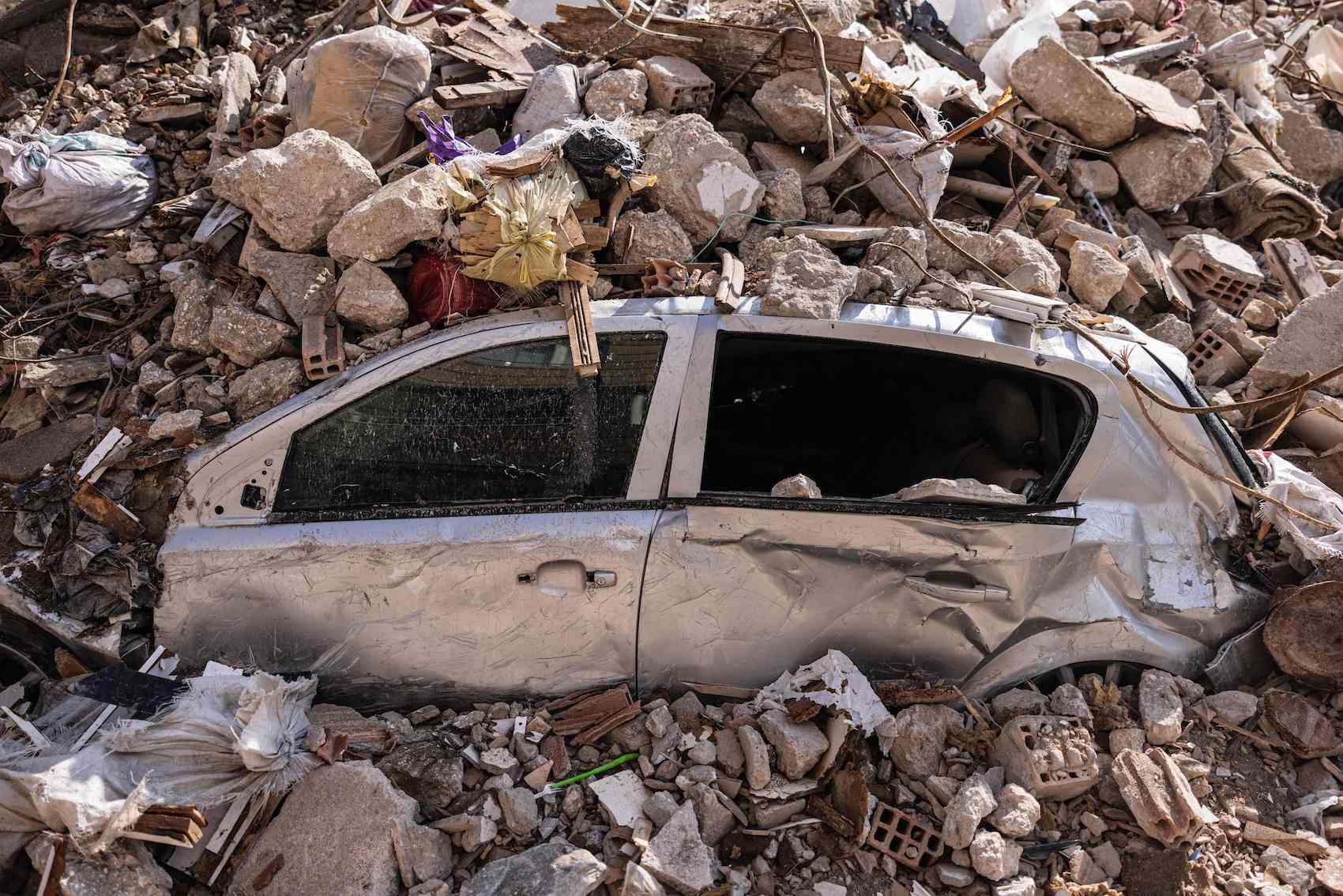 a destroyed car under the rubble of a collapsed building in Antakya