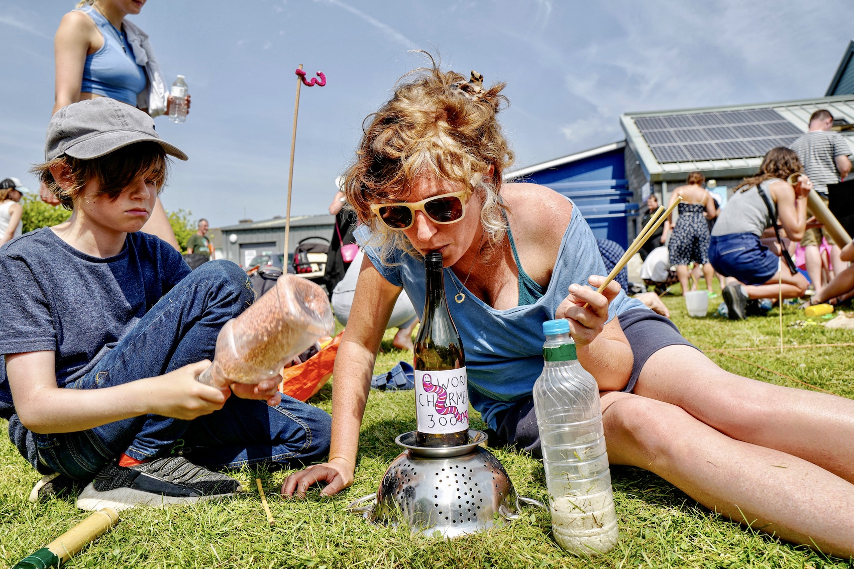 A woman competitor blowing a bottle to make sound through it into the soil and her kid beside making more sound from shaking a bottle full of small balls