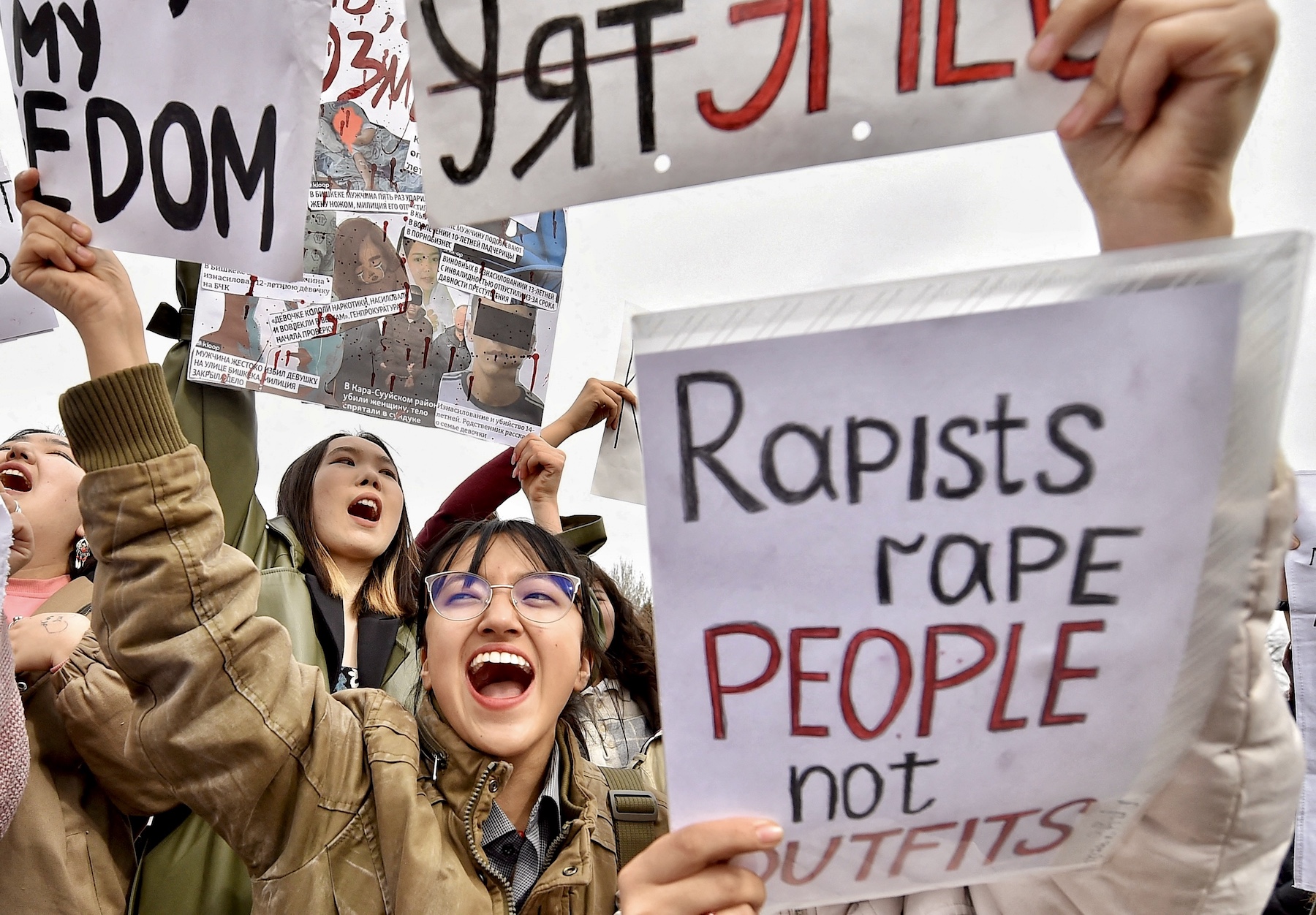 A woman appears to be shouting, and other women around her do the same. In front of her there is a sign that says, "Rapists rape people not outfits".