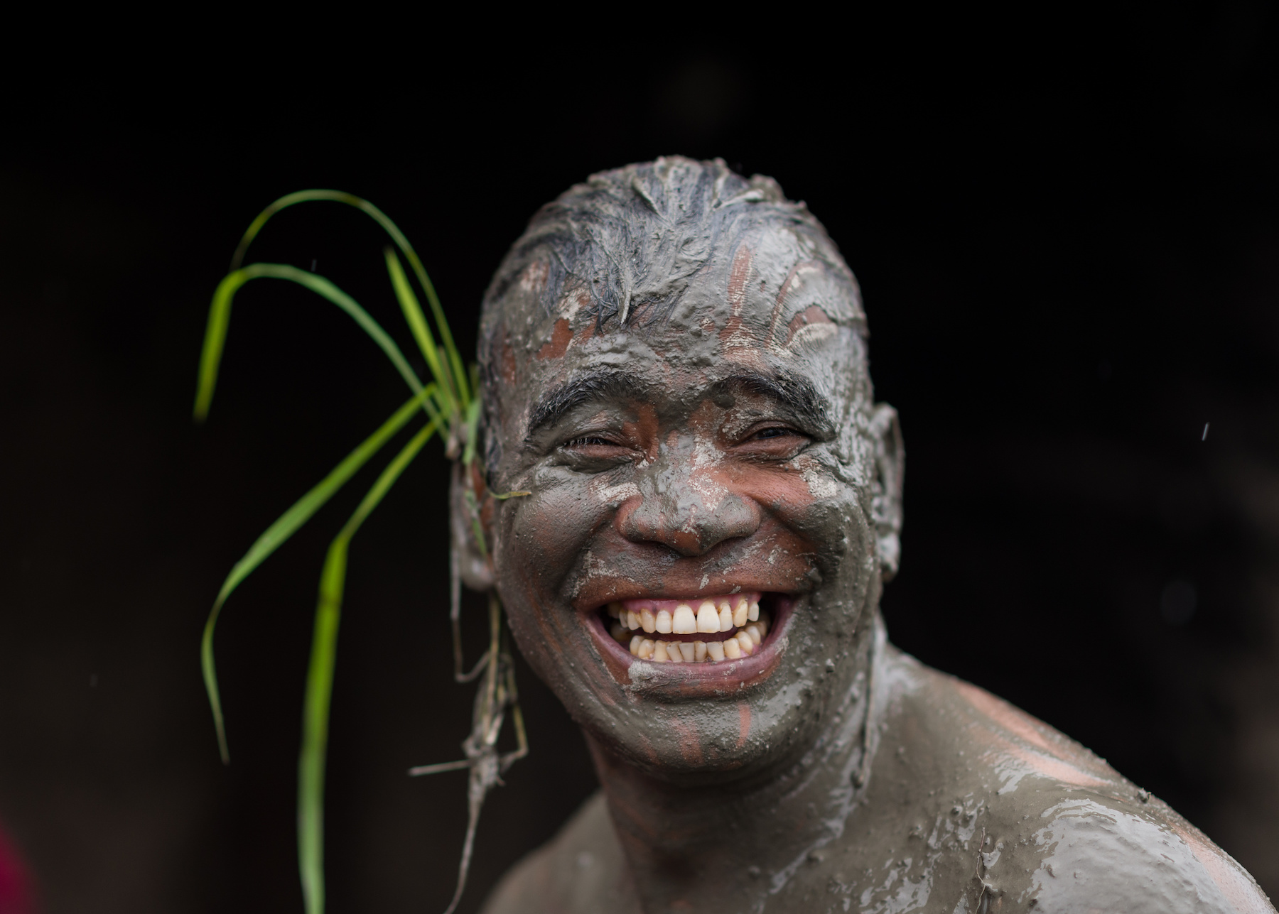 A man's face smiles while being covered in mud