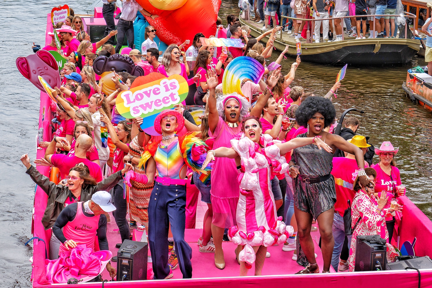 People in colorful outfits are on a boat on Amsterdam's canals celebrating Pride.