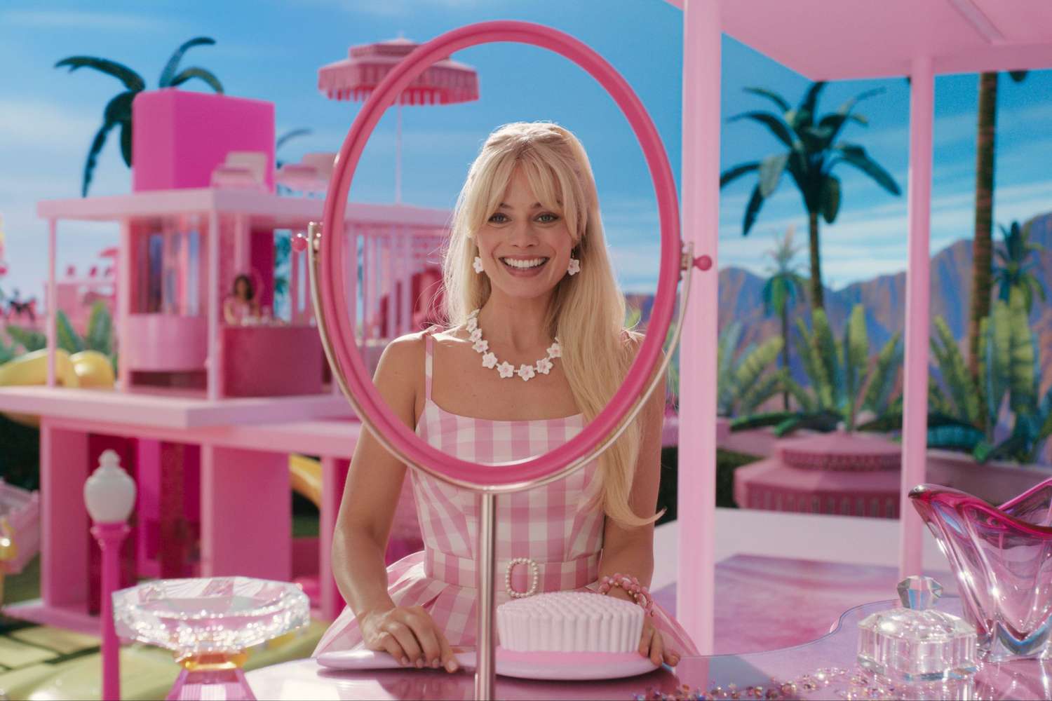 Margot Robbie, who plays Barbie, sit down in front of vanity and smiles. 