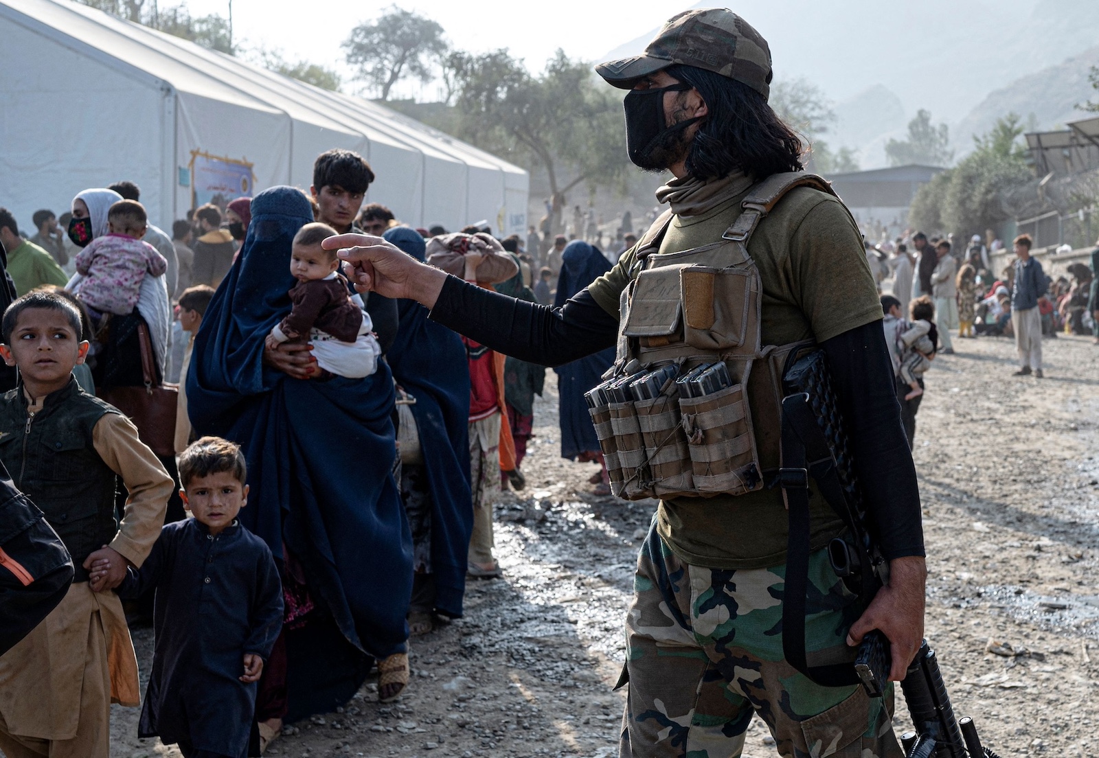 Afghan security personnel gestures as refugees arriving from Pakistan walk at the Afghanistan Pakistan Torkham border